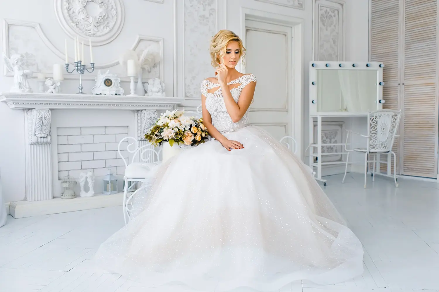 Eine Braut in einem wunderschönen Brautkleid, frisiert und geschminkt, bereitet sich auf die Hochzeit vor. Ein Porträt einer schönen jungen Frau mit blonden Haaren und blauen Augen im Studio mit Blumen.